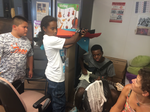 Raymond uses the glove and Justis composes music using an electric guitar. Michael and Paseo assistant director Agnes Chavez look on.